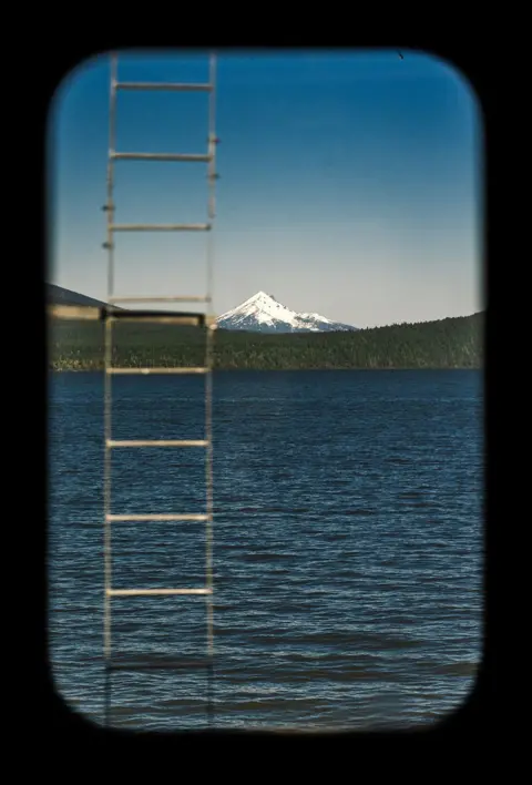 Katie Edwards A ladder coming out of a lake in front of snow capped mountains