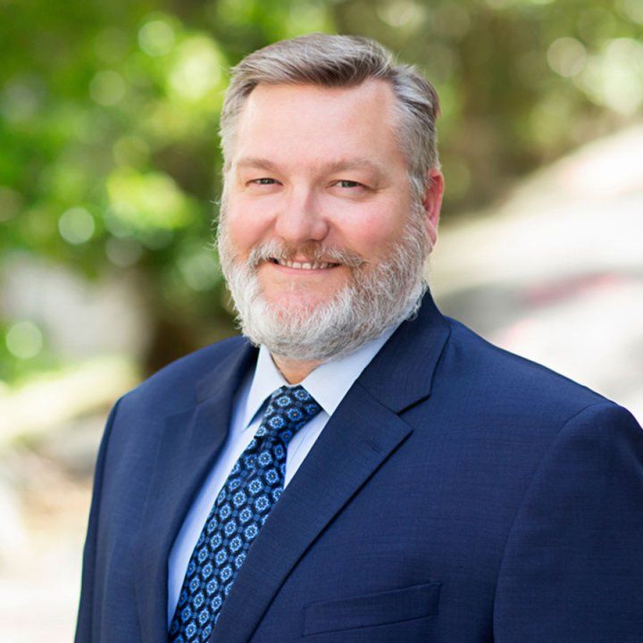 Dr. Jason Smith wearing a suit and tie. Trees are in the background.