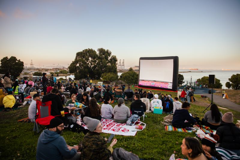 People sit on the grass in front of a screen at Sundown Cinema