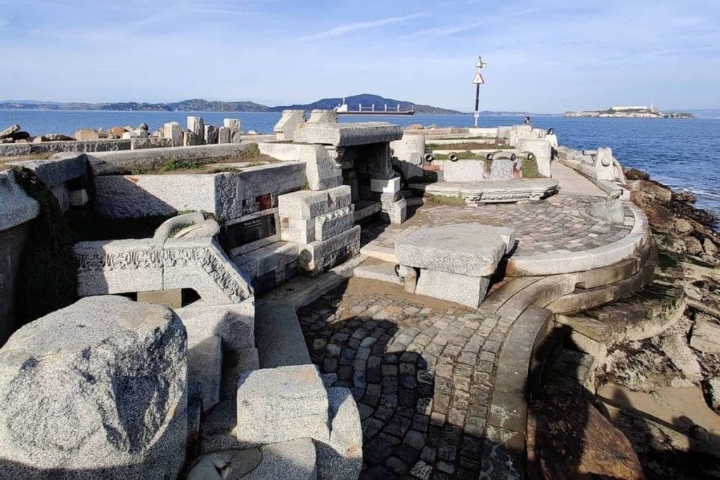 San Francisco's Wave Organ, a large outdoor sculptural structure made with large slabs of gray stone against a blue sky with clouds.