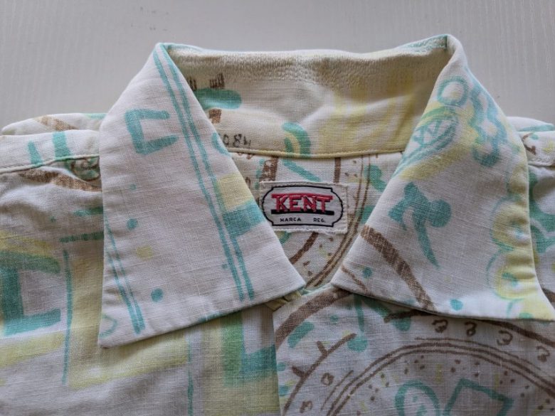 Close-up of a collared shirt with a colorful geometric pattern. The label reads 