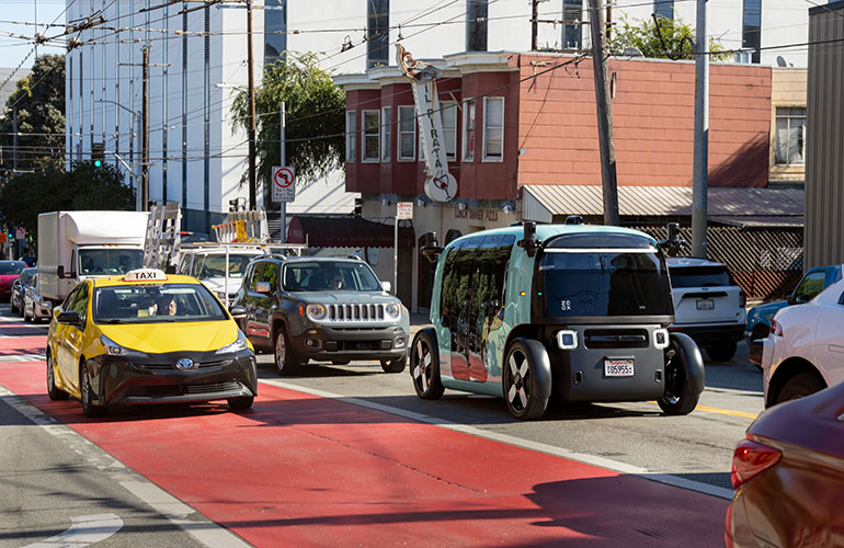 One of Zoox's purpose-built robotaxis, a small, boxy vehicle with no front or back, driving down a road in Las Vegas. 